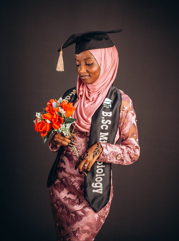 A young African female graduate in hijab holding a bouquet, celebrating her achievement.